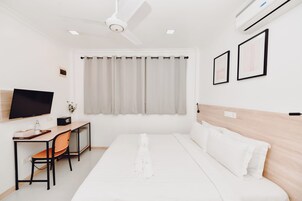 Habitación de hotel con cama, escritorio con silla, televisor y ventilador de techo.