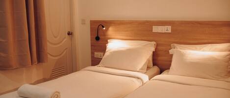 A hotel room with two beds, a wooden headboard, a wall-mounted light, and a door with a curtain.