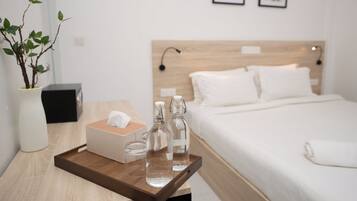 A hotel room with a wooden headboard, a neatly made bed, a bedside table with a tissue box, two glass bottles, and a vase with a plant.
