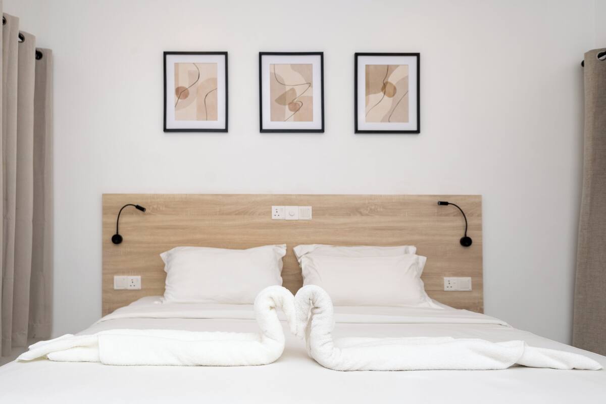 A hotel room with a wooden headboard, white bedding, and three framed abstract artworks on the wall.