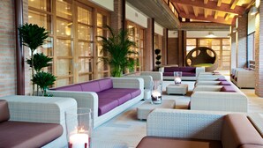 A modern lounge area with wicker furniture, a large cushioned sofa, and a round seating area. - Green Village Eco Resort (Lignano Sabbiadoro)