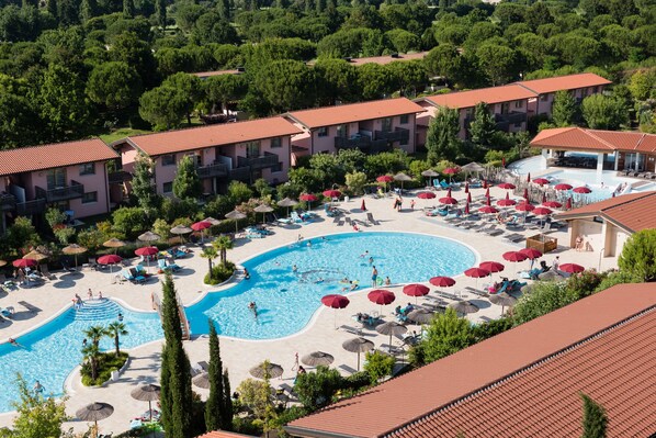 A resort with multiple buildings, a central swimming pool, and numerous sun loungers and umbrellas. - Green Village Eco Resort (Lignano Sabbiadoro)