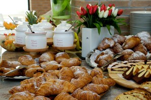 A buffet spread with various pastries, including croissants and cakes, and a vase of red and white tulips. - Green Village Eco Resort (Lignano Sabbiadoro)