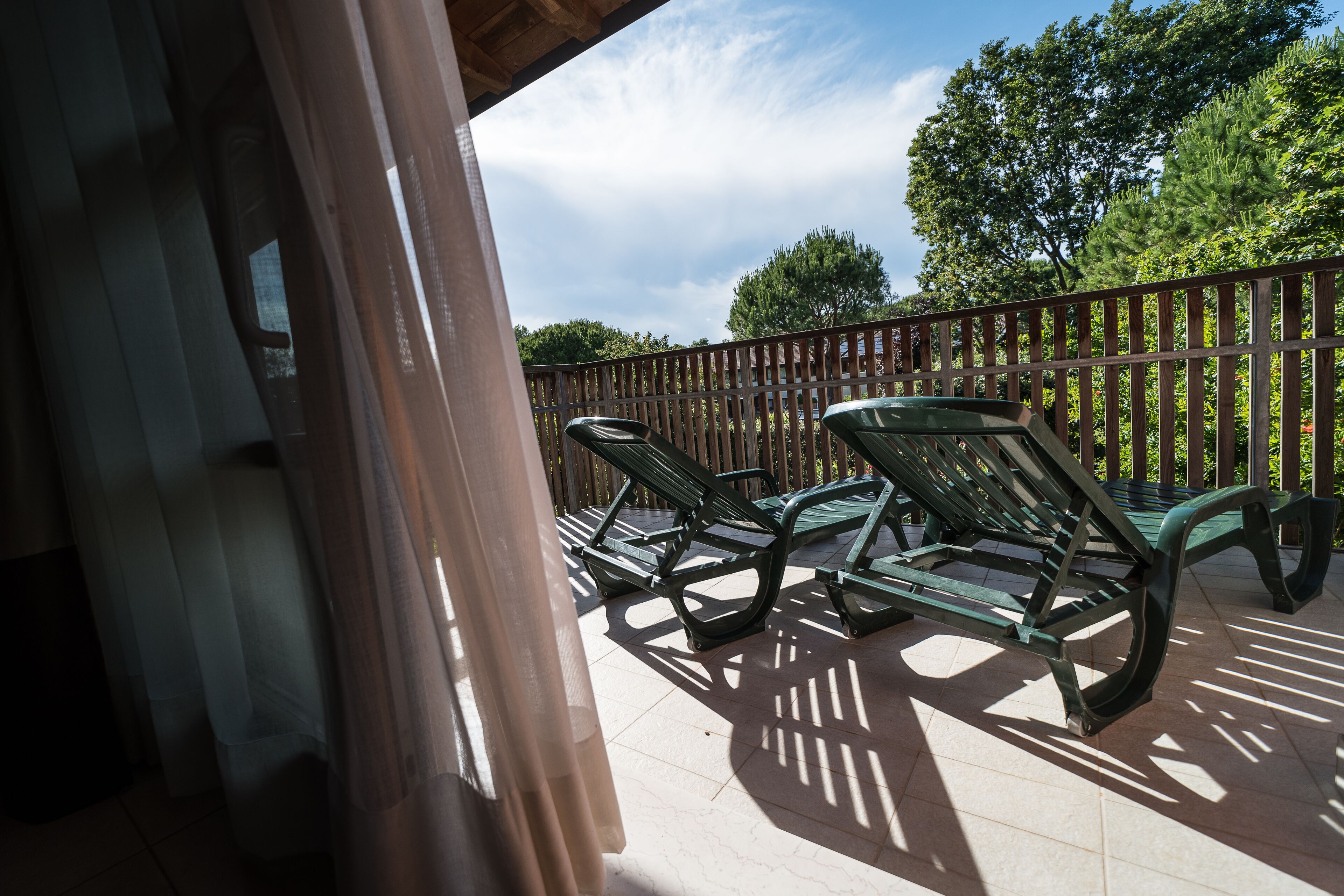 A covered outdoor area with two green lounge chairs and a wooden fence.