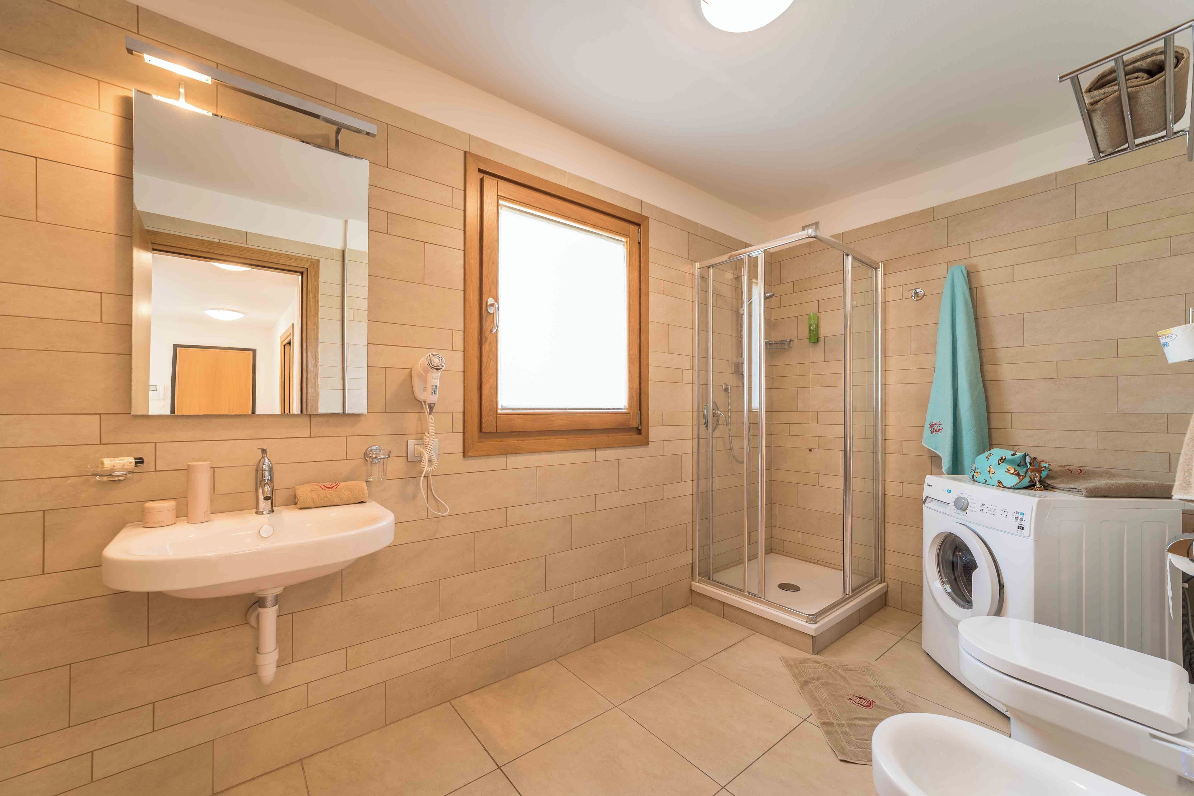 A bathroom with a sink, mirror, shower, and washing machine.