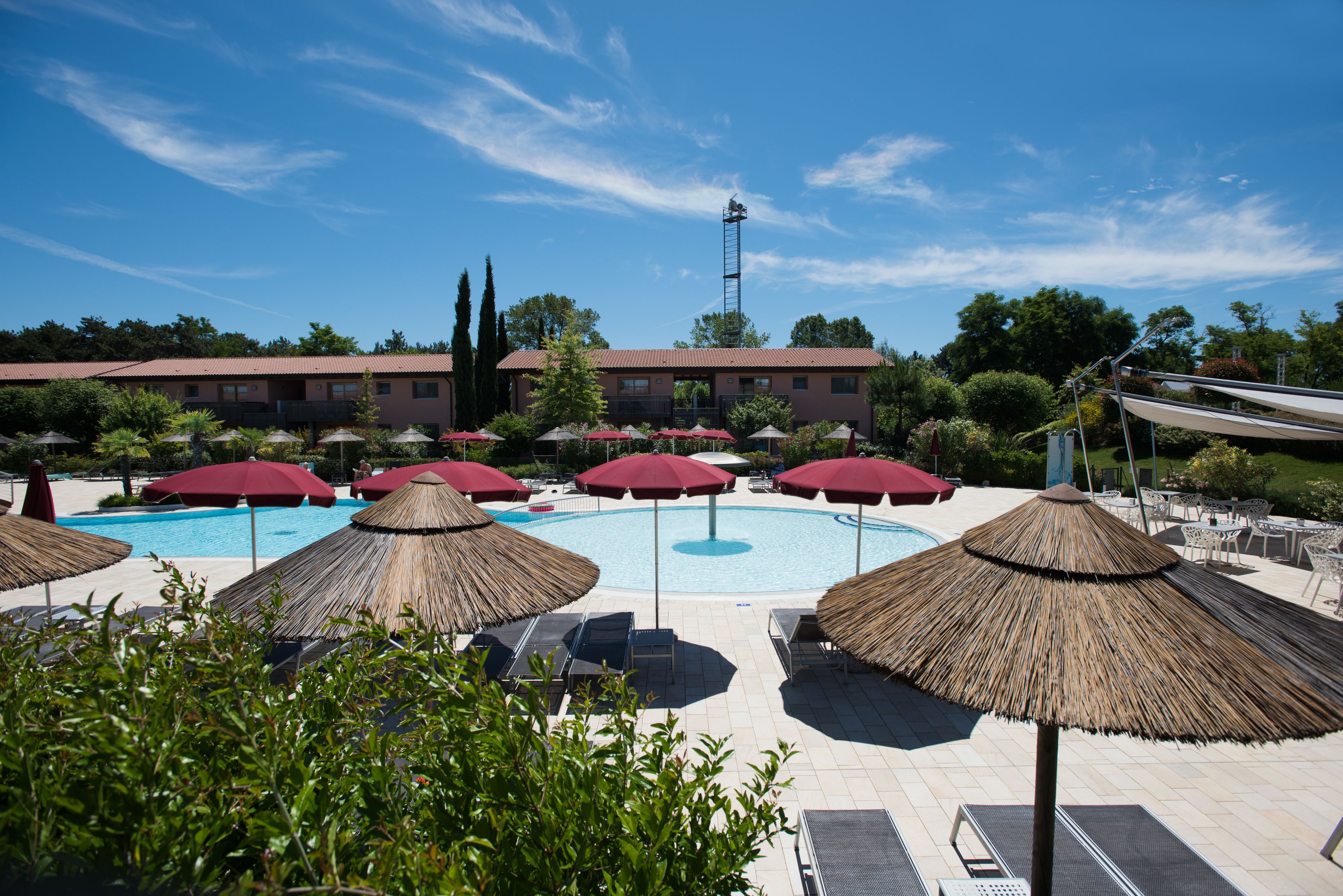 Ein Poolbereich mit Sonnenschirmen, Liegestühlen und einem Gebäude im Hintergrund.