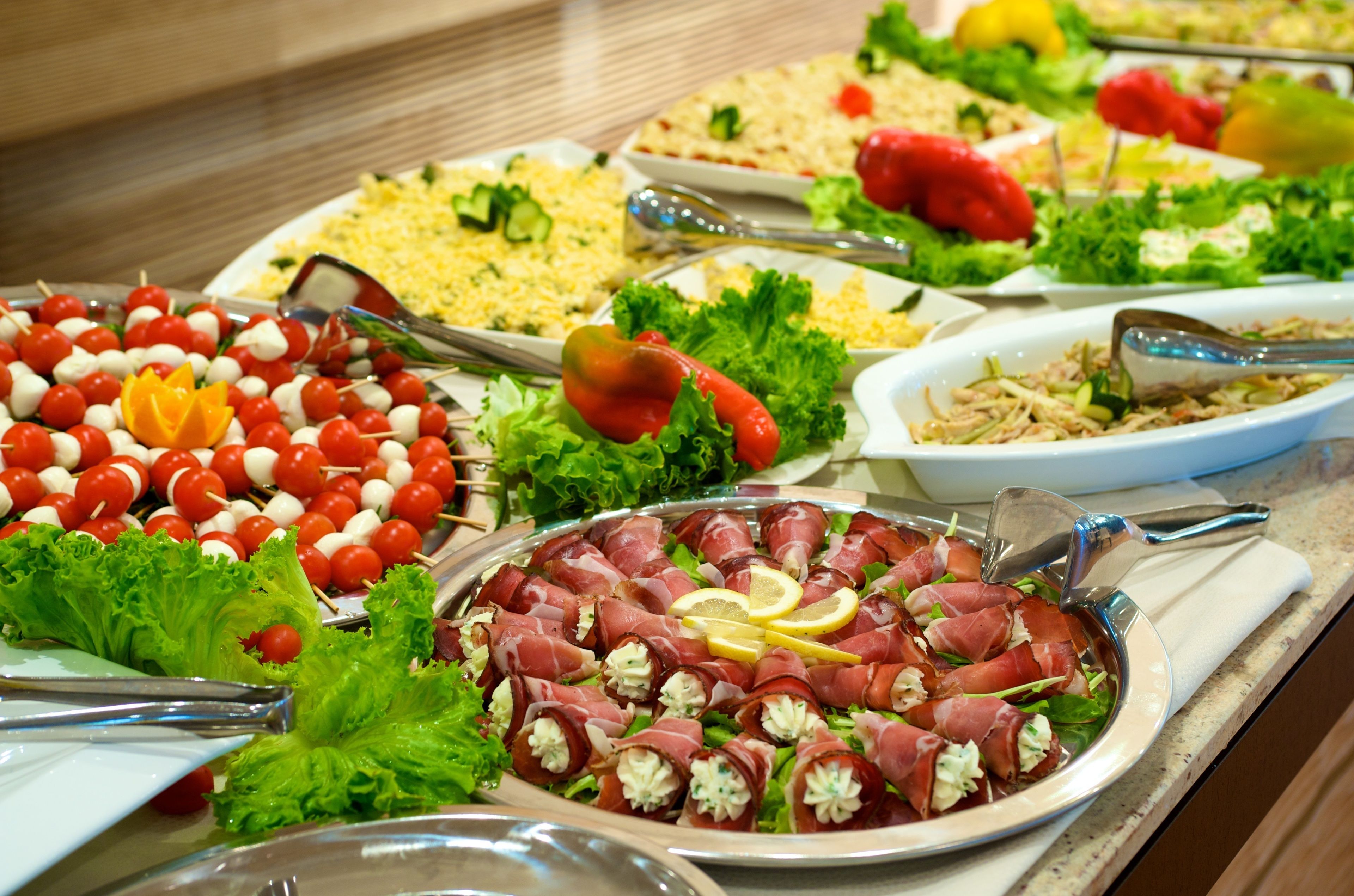 Ein Buffet mit verschiedenen Gerichten, darunter Spieße, Salate und eine Platte mit Prosciutto-Wraps.