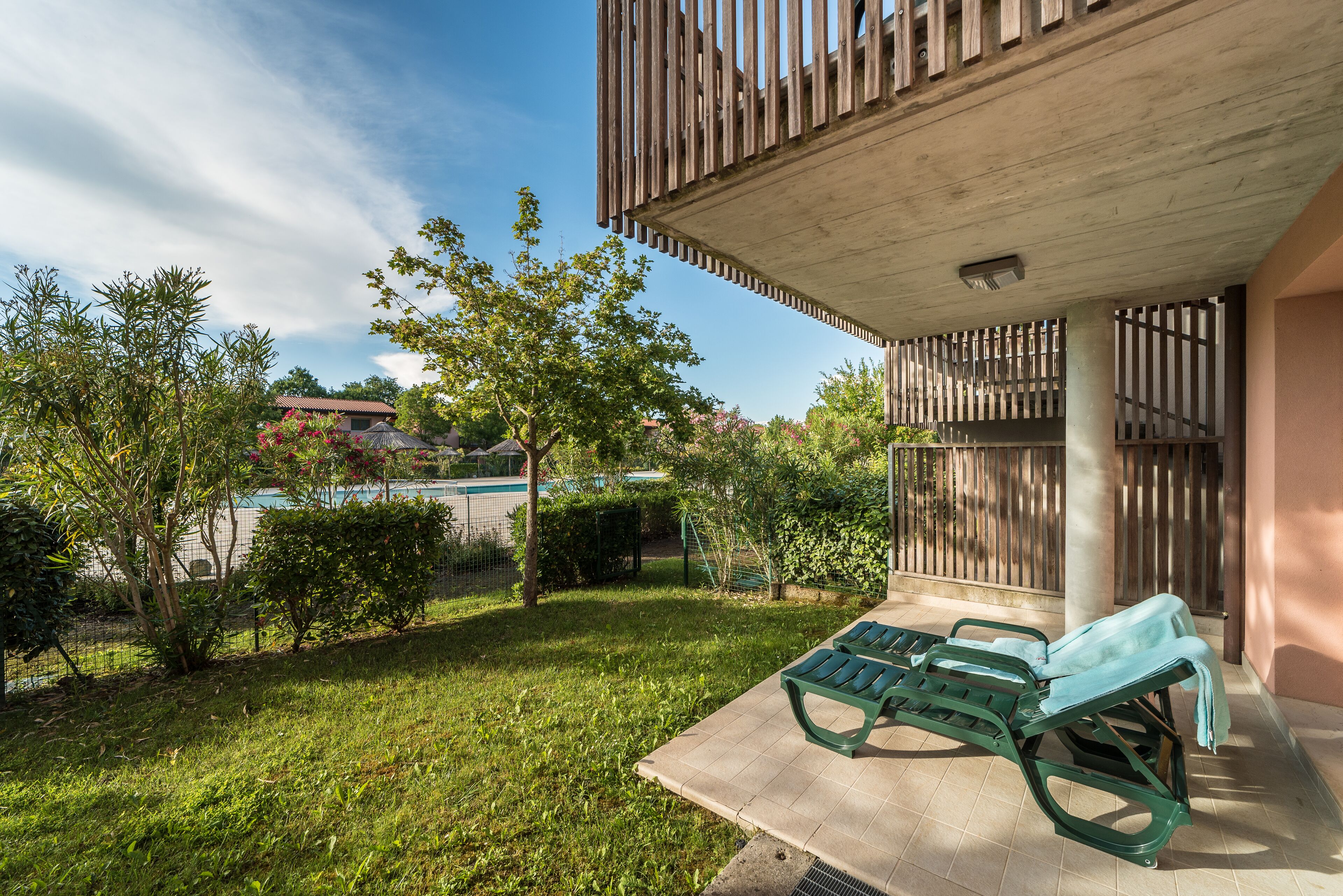 A patio area with two green lounge chairs, a pool, and a view of a residential building in the background.