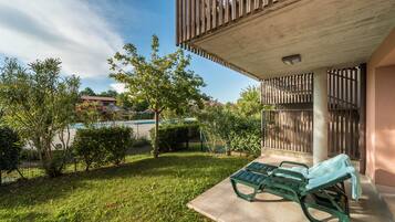 A patio area with two green lounge chairs, a pool, and a view of a residential building in the background.