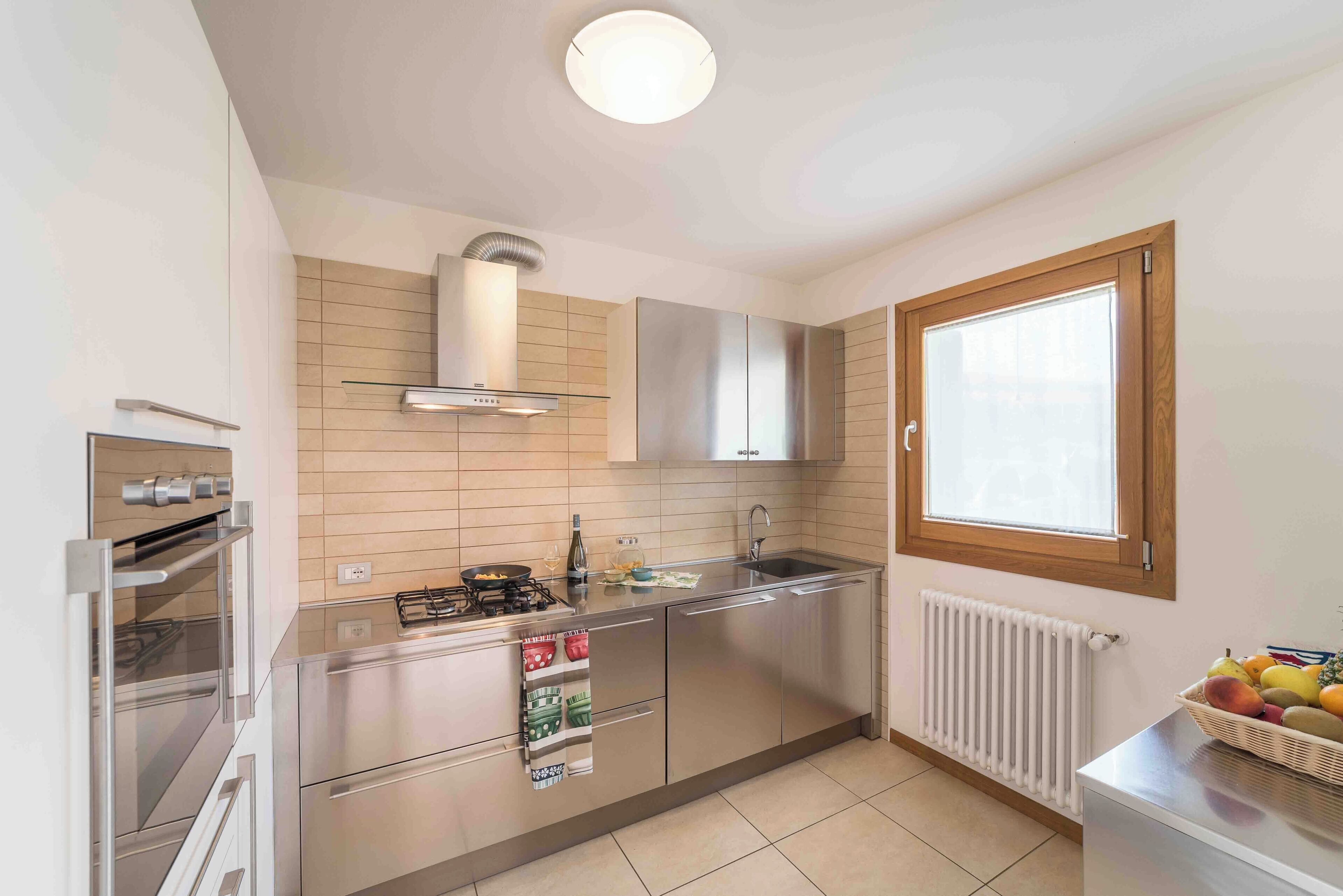 A modern kitchen with stainless steel appliances, a window, and a radiator.