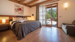 A bedroom with a large bed, wooden flooring, a nightstand with a lamp, a wall-mounted artwork, and a sliding glass door leading to an outdoor area. - Green Village Eco Resort (Lignano Sabbiadoro)