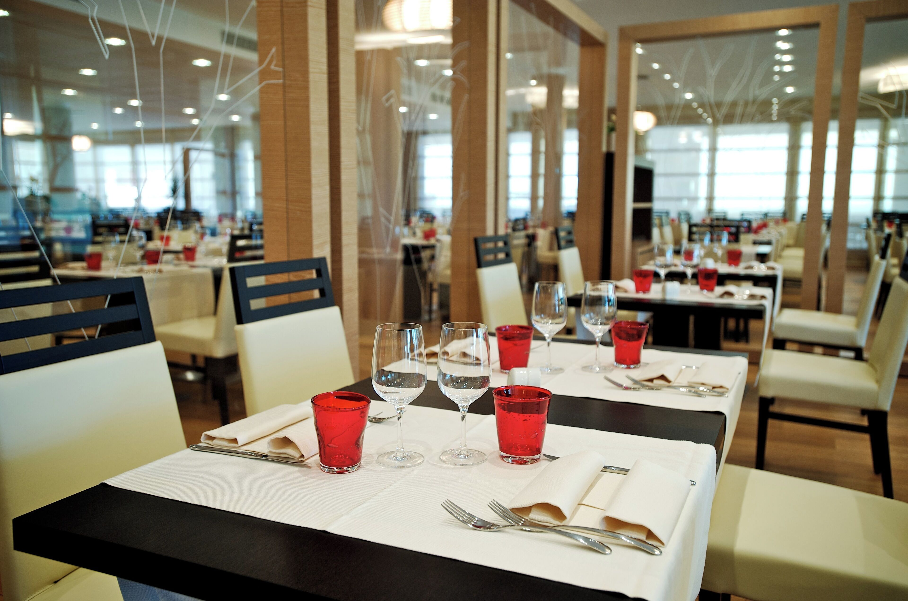 Ravintola, jossa on katetut ruokapöydät, punaiset lasit ja valkoiset servetit.