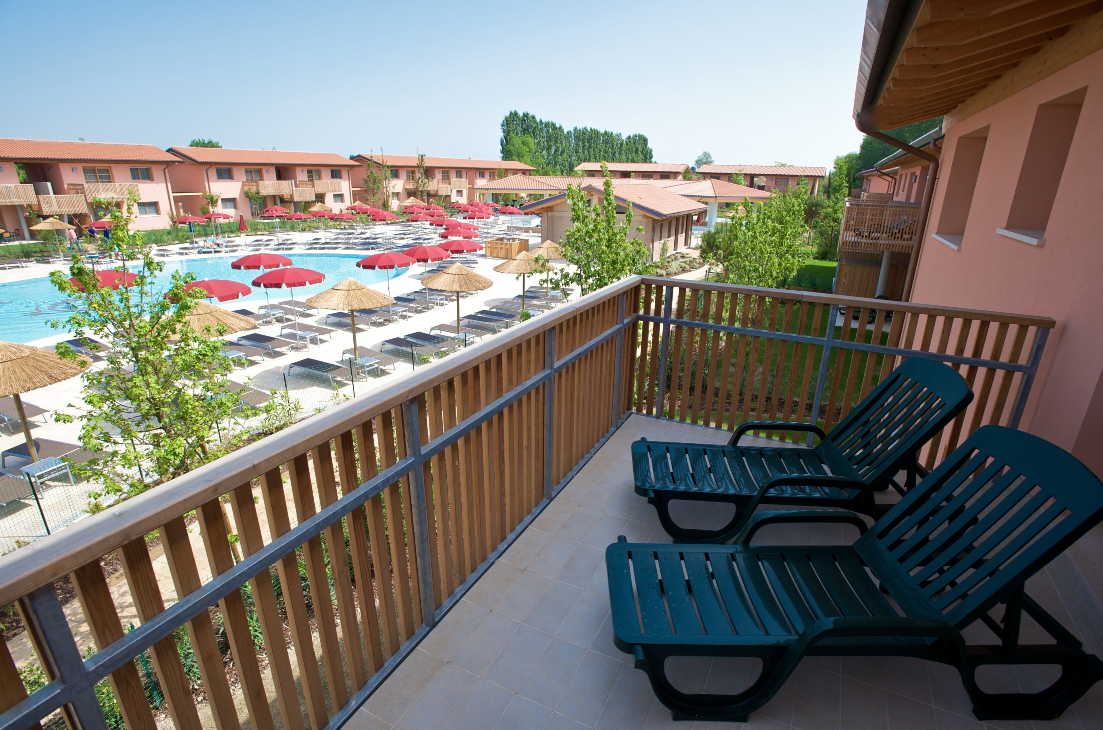 Balcón con vista a un área de piscina, incluyendo sillones y sombrillas.