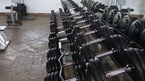 Un gimnasio con hileras de mancuernas y discos de pesas, una prensa de banca y una estructura para sentadillas.