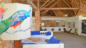 Un espacio al aire libre con techo amoblado con sofás blancos y cojines azules, un pilar de piedra y una escultura de un pájaro colorido.