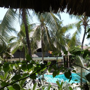 A pool surrounded by palm trees and a thatched roof structure. - Aquarius Club International Resort (Watamu)