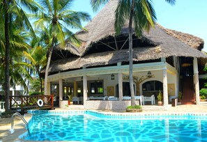 A resort with a pool, thatched-roof structure, palm trees, and a stone wall. - Aquarius Club International Resort (Watamu)