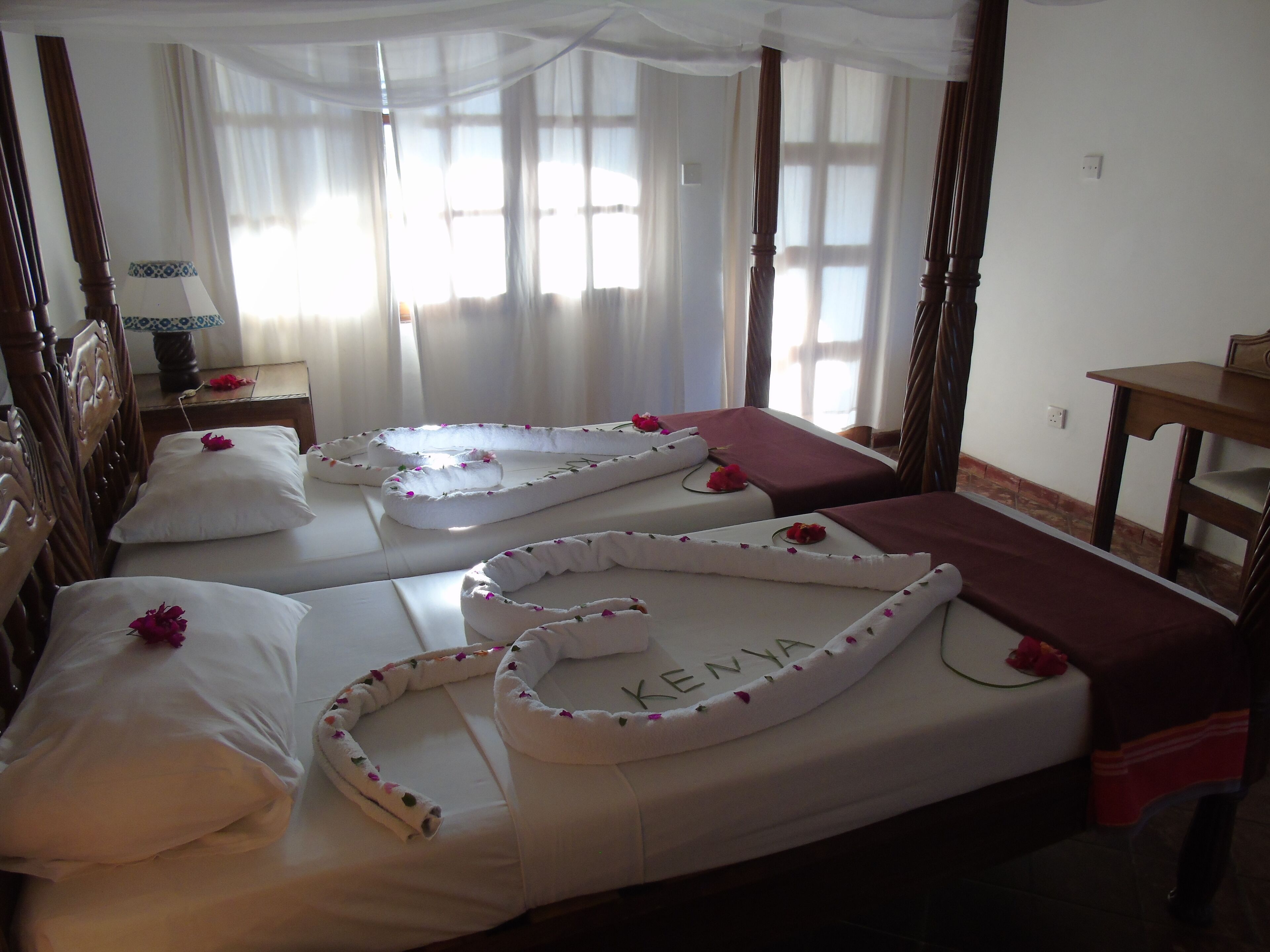 A hotel room with two beds, each adorned with white linens and pink flowers.
