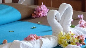 Una cama bien hecha con una colcha azul, toallas blancas y un ramo de flores.