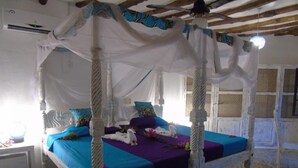 Una cama con dosel y cuatro columnas, con barandales blancos y una colcha azul y morada.