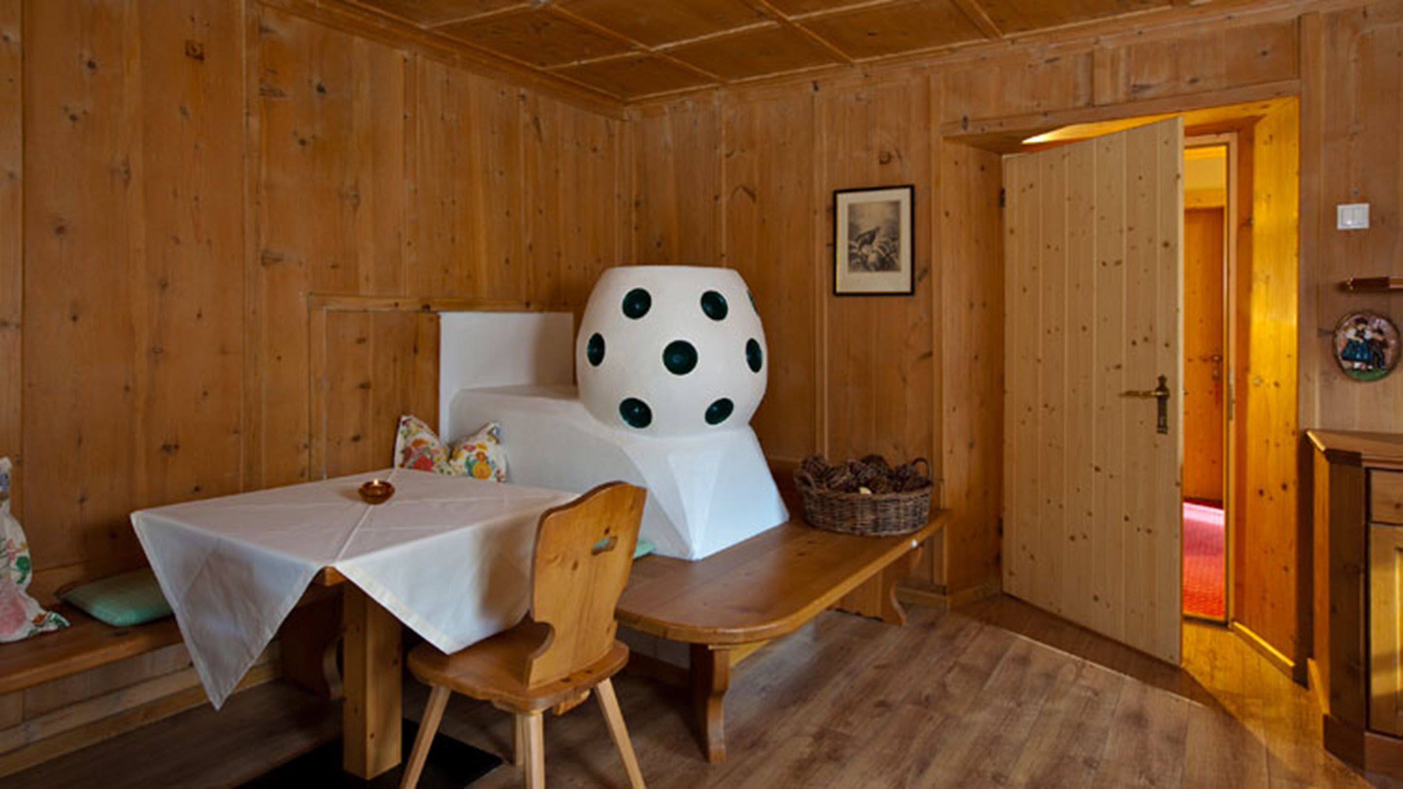 Ein Zimmer mit Holzboden, einem Bett, einem Tisch und einem Stuhl. Eine Tür führt in einen anderen Raum.
