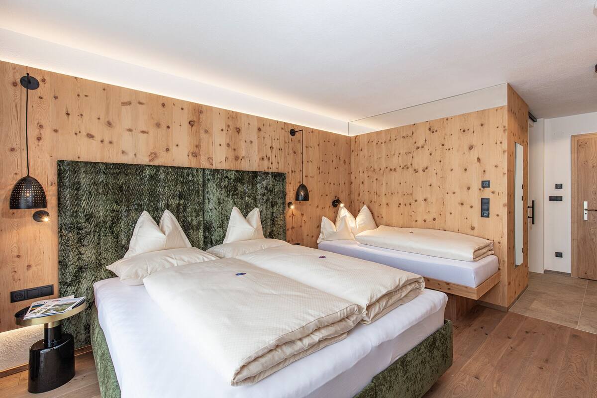 Ein modernes Hotelzimmer mit zwei Betten, Holzvertäfelung und einem grün strukturierten Kopfteil.