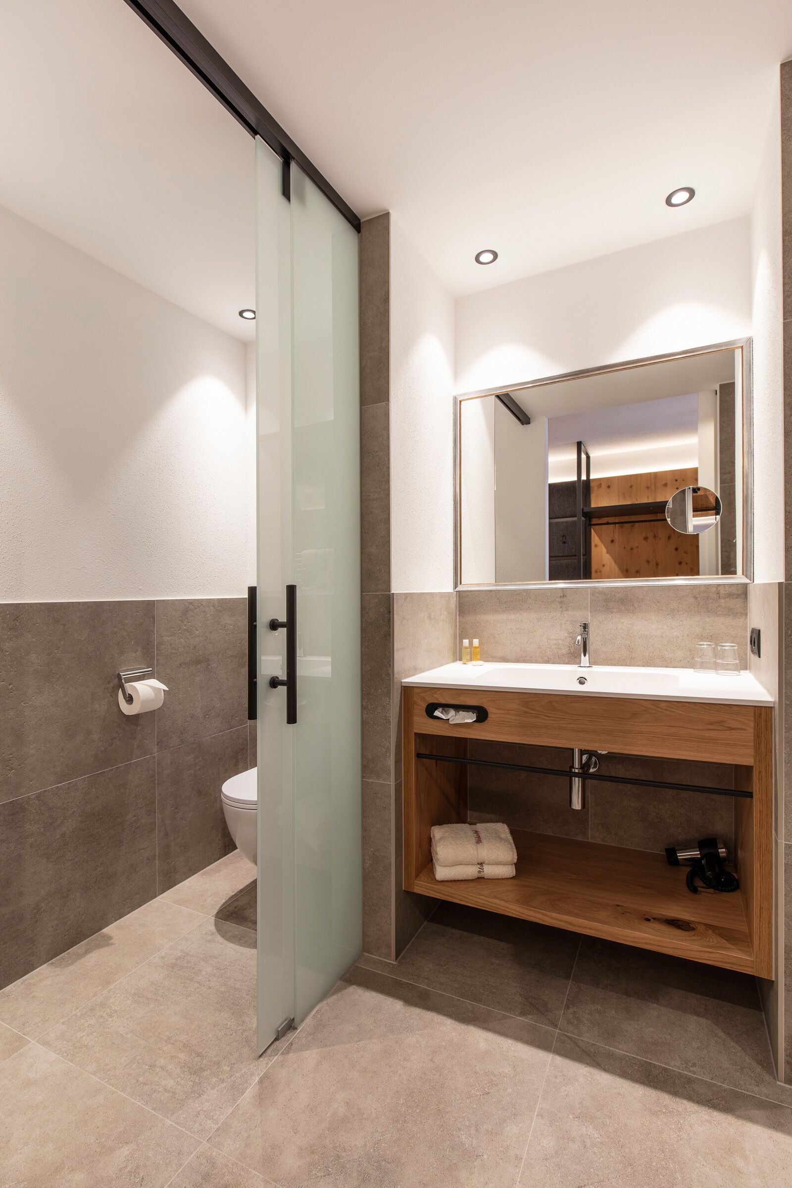 A modern bathroom with a glass shower door, a wooden vanity, and a large mirror.