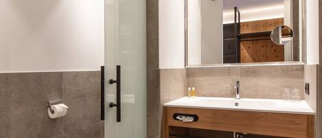 A modern bathroom with a glass shower door, a wooden vanity, and a large mirror.