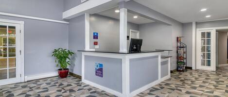 Un área de recepción con mostrador de registro, una planta en maceta y suelo de baldosas.
