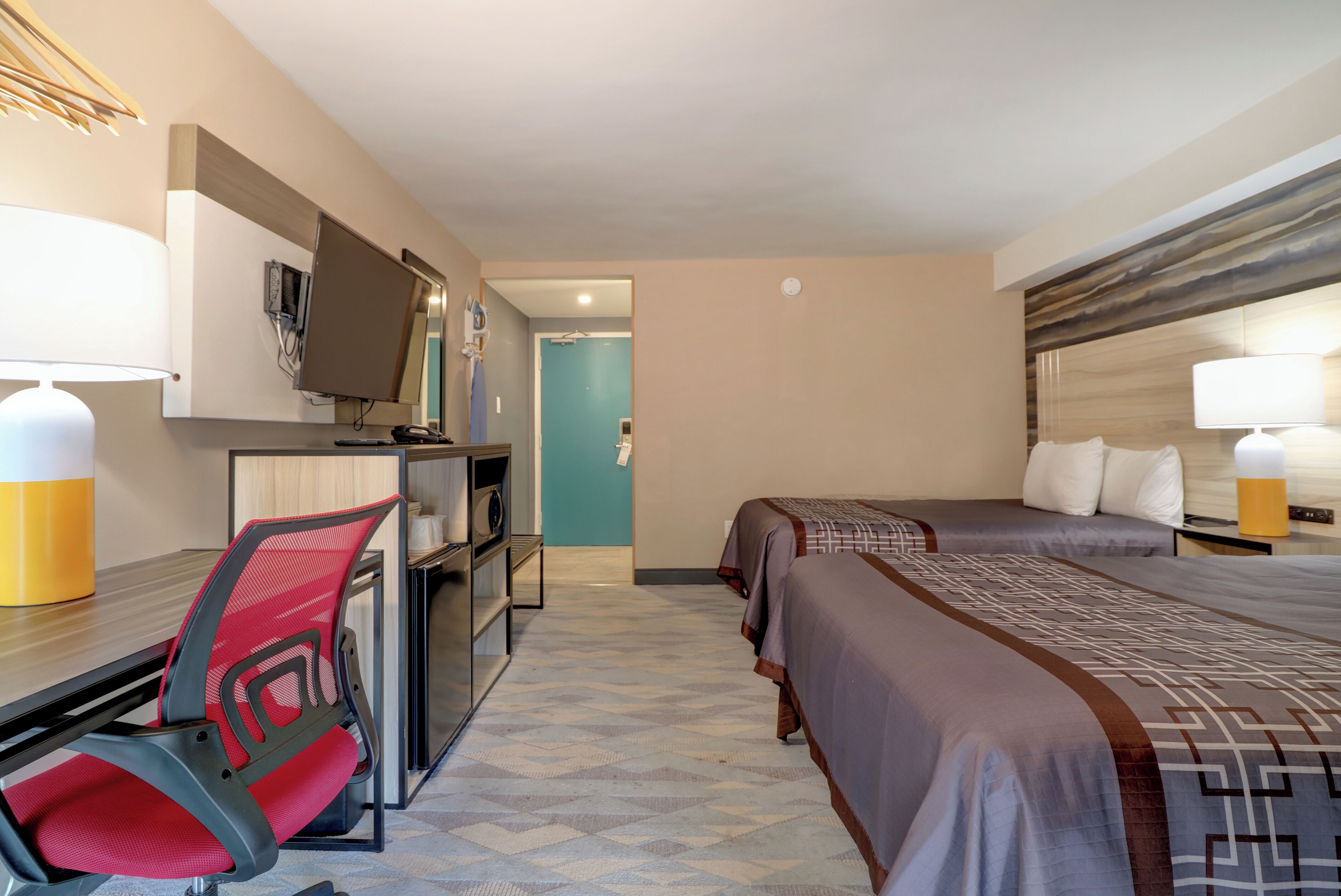 Ein Hotelzimmer mit Schreibtisch, zwei Betten, Fernseher und Lampe.