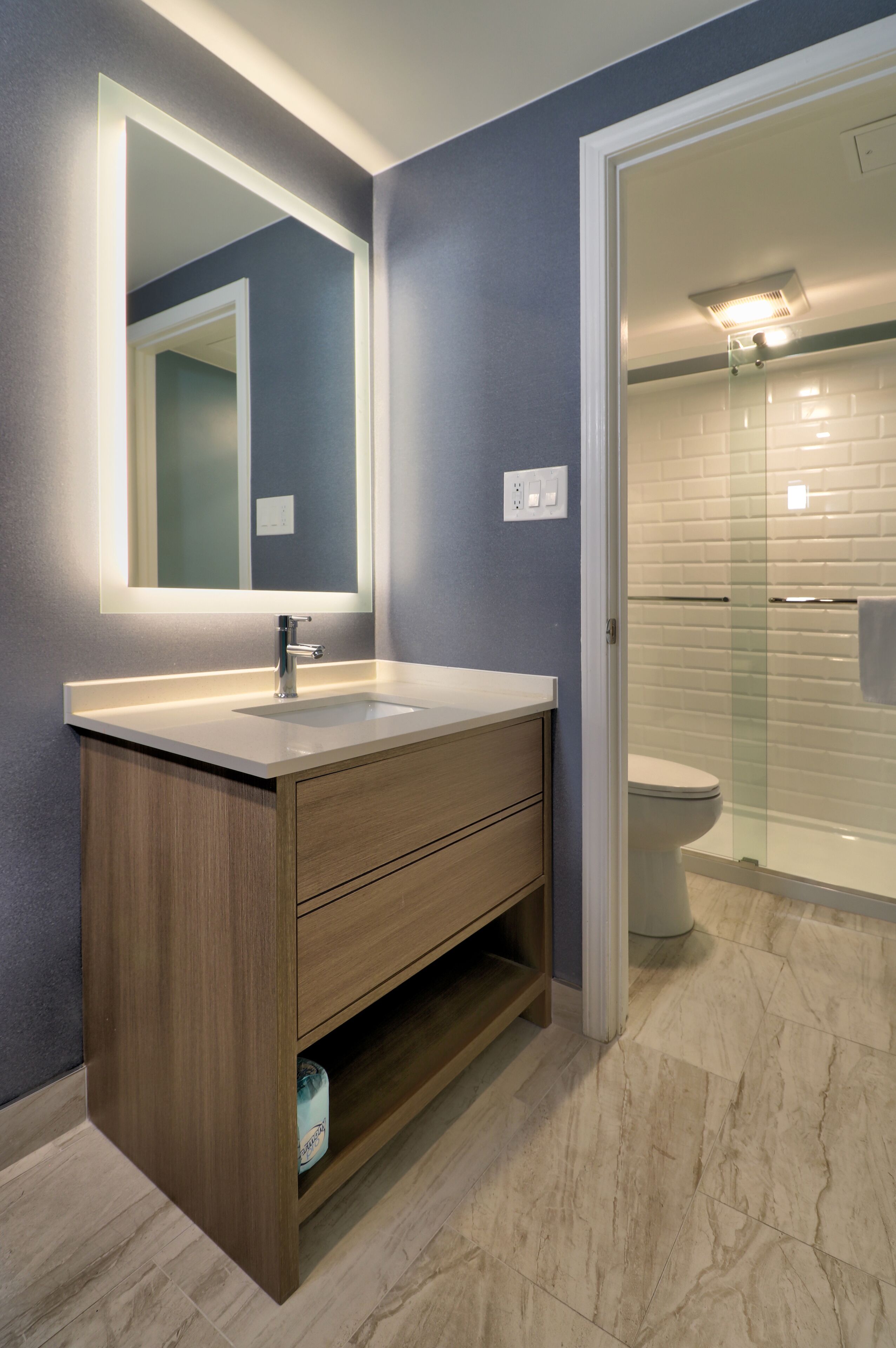 A modern bathroom with a wooden vanity, a large mirror, and a glass-enclosed shower.