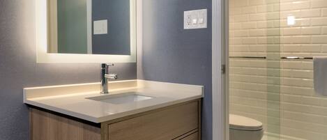A modern bathroom with a wooden vanity, a large mirror, and a glass-enclosed shower.