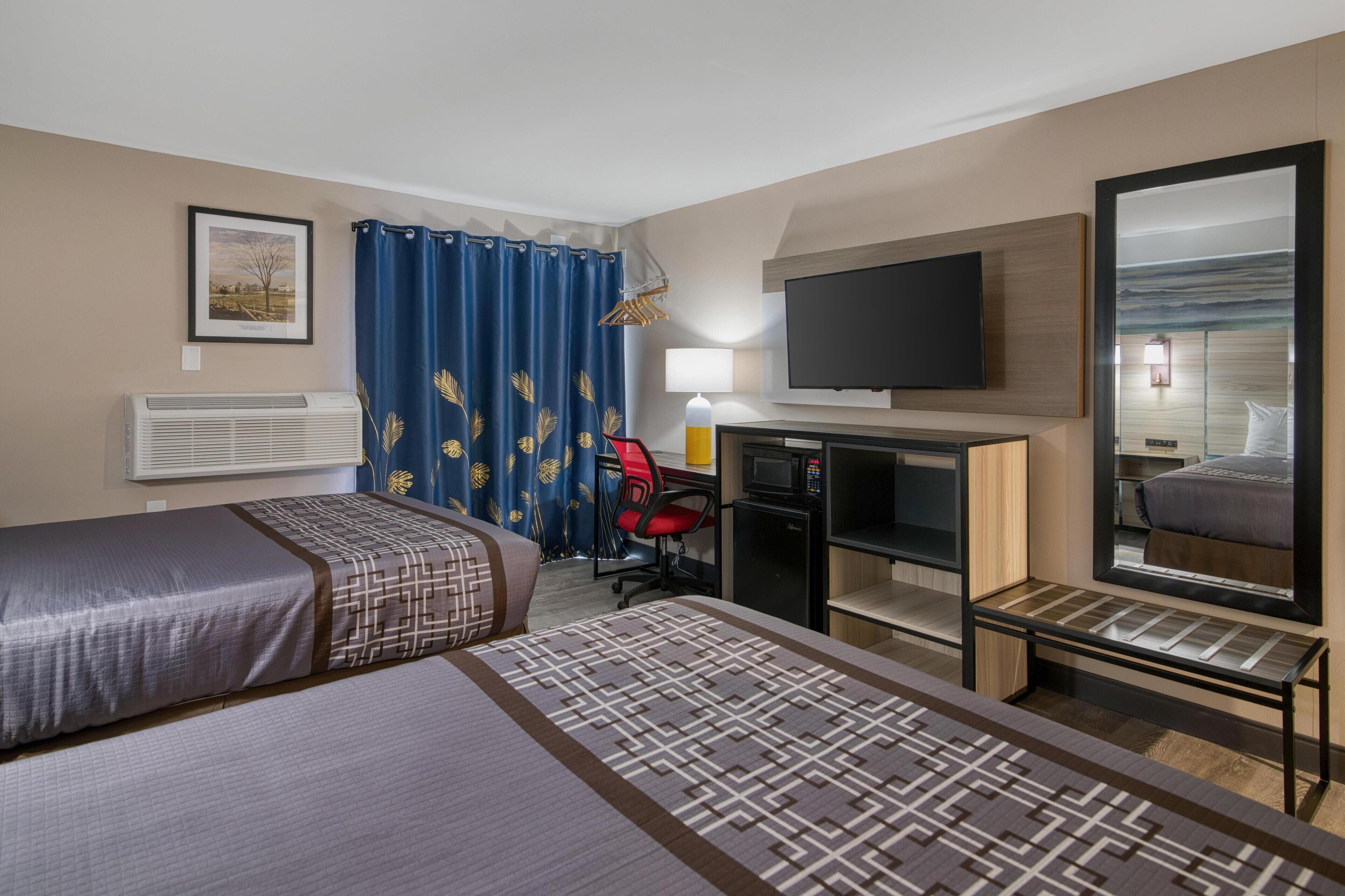 A hotel room with two beds, a desk with a computer, a TV, a mirror, and a window with a view.