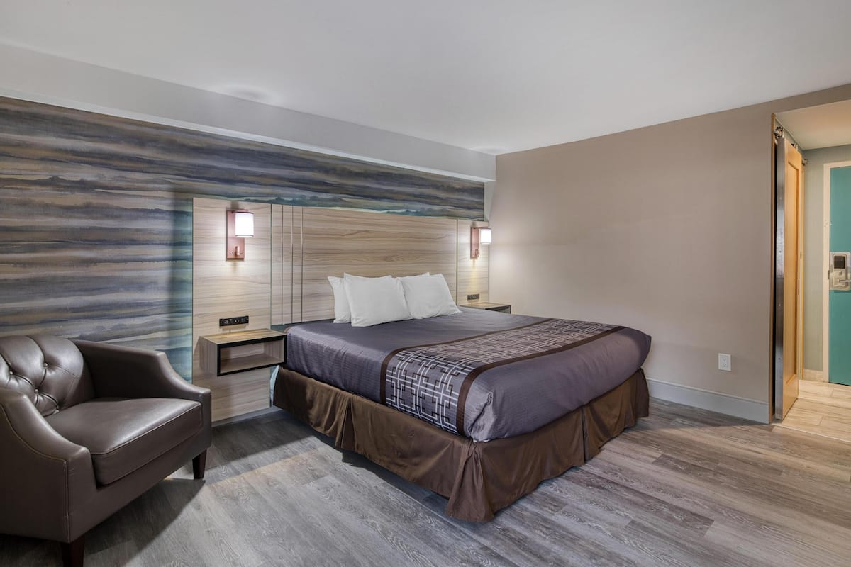 A modern bedroom with a large bed, a leather armchair, and a wooden headboard.