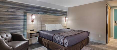 A modern bedroom with a large bed, a leather armchair, and a wooden headboard.