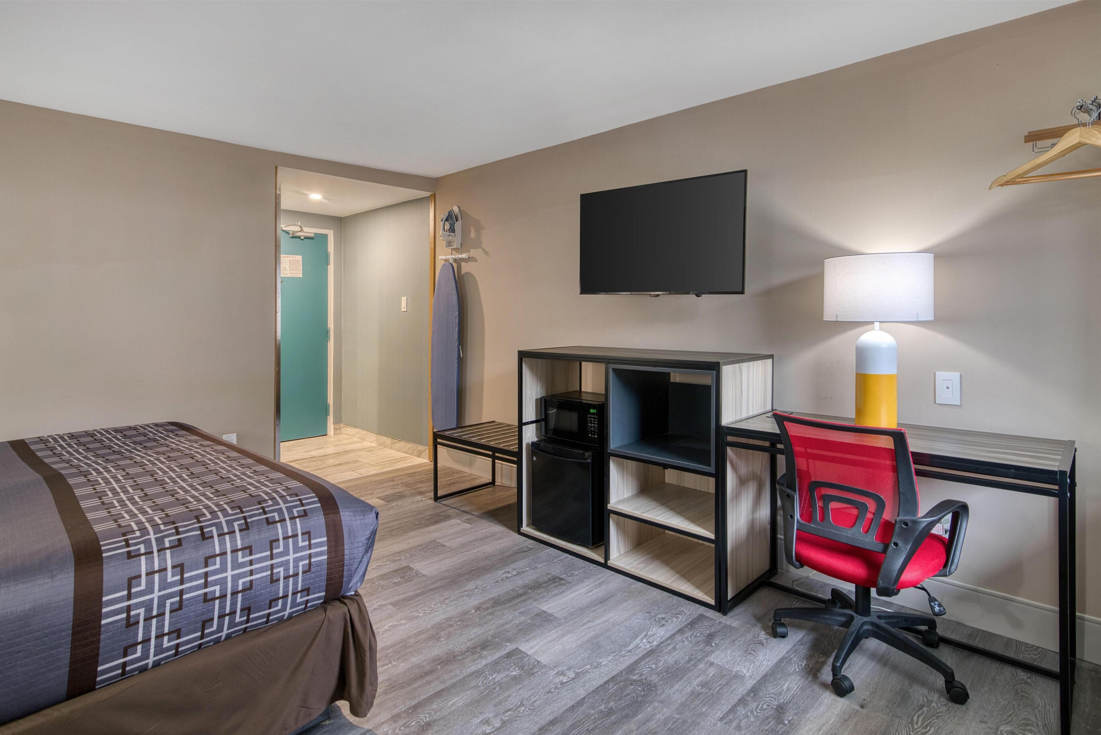 Una habitación de hotel con cama, escritorio con computadora, silla, televisor y lámpara.
