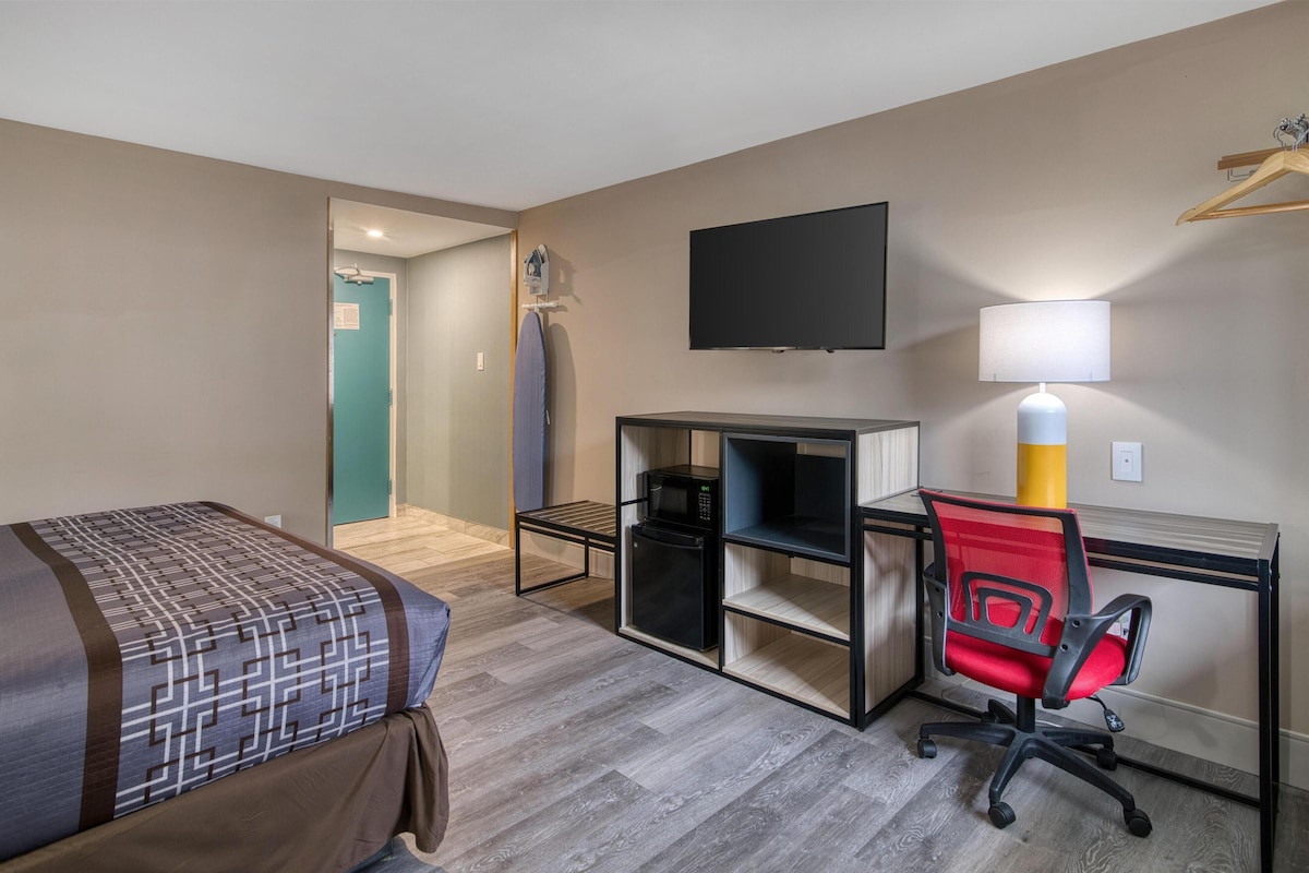 Une chambre d’hôtel avec un lit, un bureau avec un ordinateur, une chaise, une télévision et une lampe.