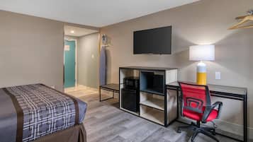 Una habitación de hotel con cama, escritorio con computadora, silla, televisor y lámpara.