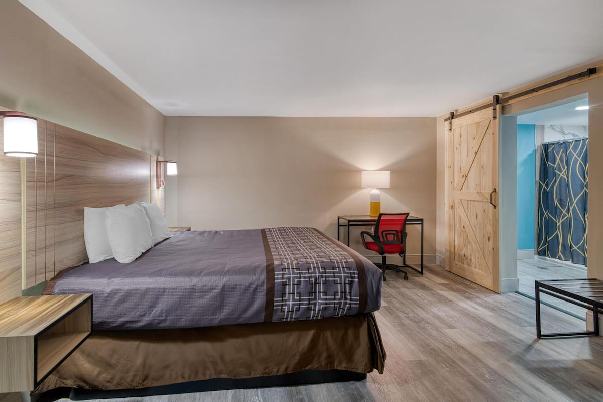 A hotel room with a bed, bedside table, lamp, chair, and a sliding door leading to a bathroom.