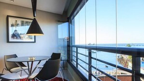 A modern room with a large window overlooking a body of water, a round table with chairs, and a pendant light. - Flat Iate (Fortaleza)