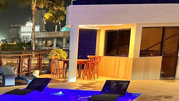 An outdoor pool area with lounge chairs, a wooden table, and chairs. - Flat Iate (Fortaleza)
