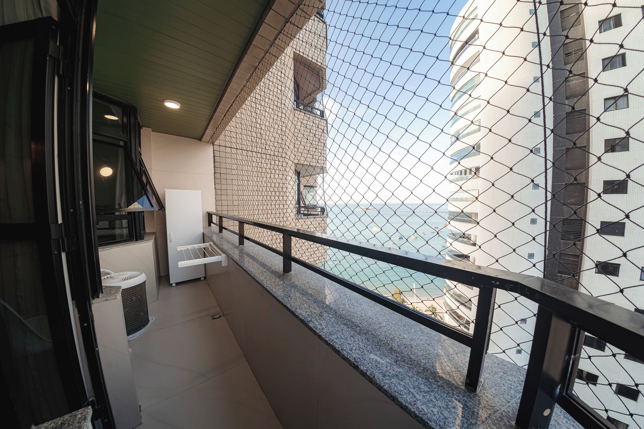 A balcony with a view of the sea, a white chair, and a small table.
