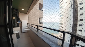 A balcony with a view of the sea, a white chair, and a small table.