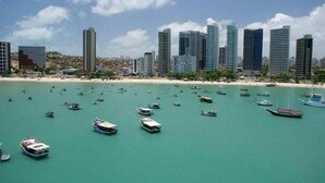 A coastal cityscape with numerous high-rise buildings and a beach with boats in the water. - Flat Golden Fortaleza (Fortaleza)