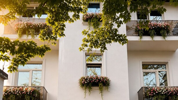 En bygning med skilt der viser 'Vela Maria', en scooter parkeret ved indgangen, og blomsterkasser på balkonerne.