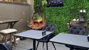 En udendørs patio med hængestol, to borde og kaffestation.