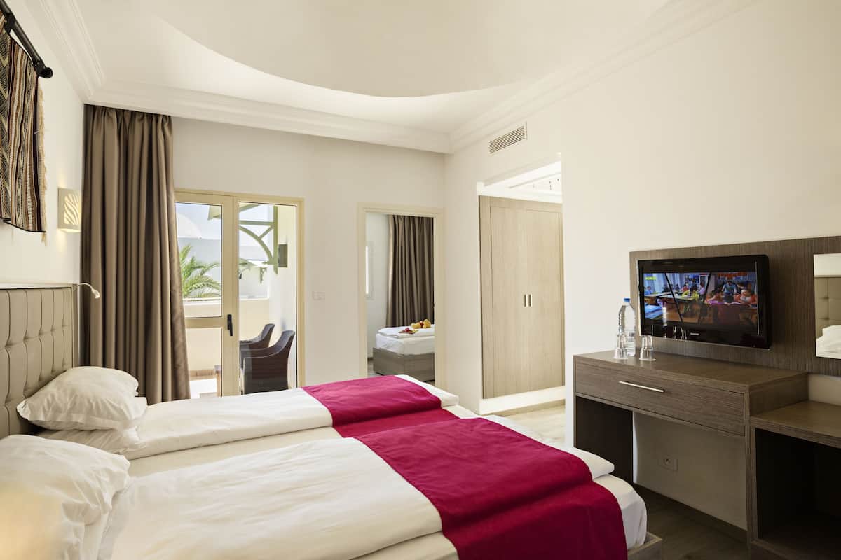 A hotel room with two beds, a television, a desk, and a view of the outdoors.
