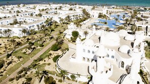 An aerial view of a coastal resort with white buildings, palm trees, and a large pool area. - ROBINSON DJERBA BAHIYA - All inclusive (Aghir)