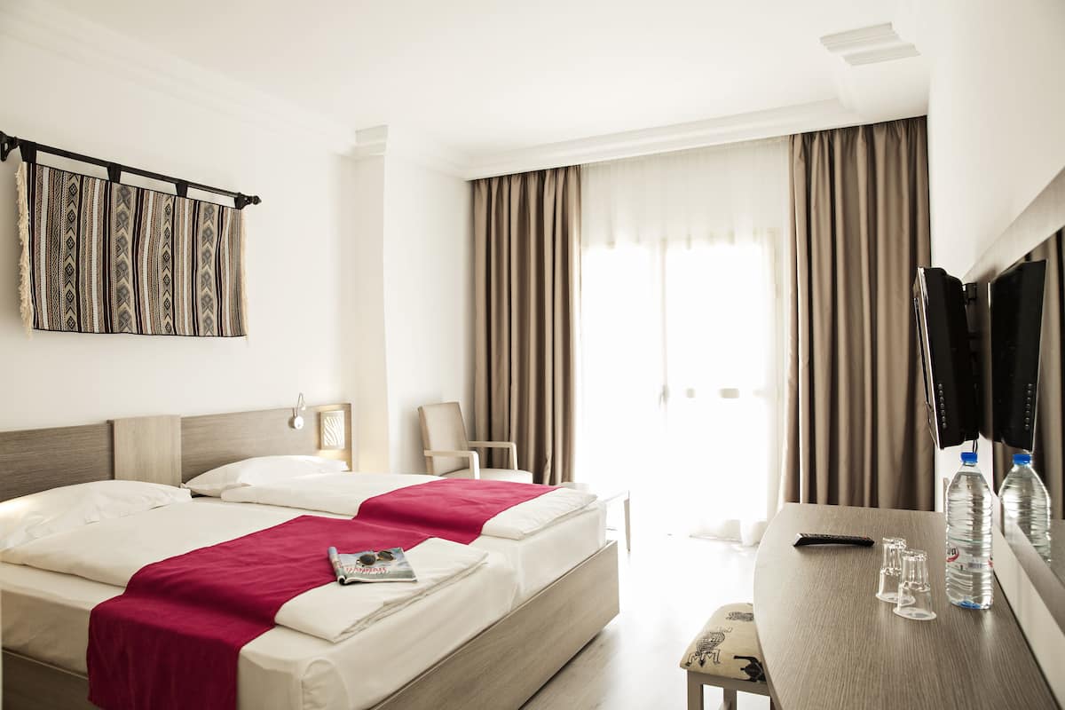 A hotel room with two beds, a TV, a desk with a mirror, and a window with curtains.