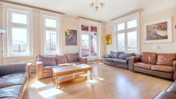 A spacious living room with leather sofas, a wooden coffee table, large windows, and artwork on the walls. - Hootananny Hostel (London)